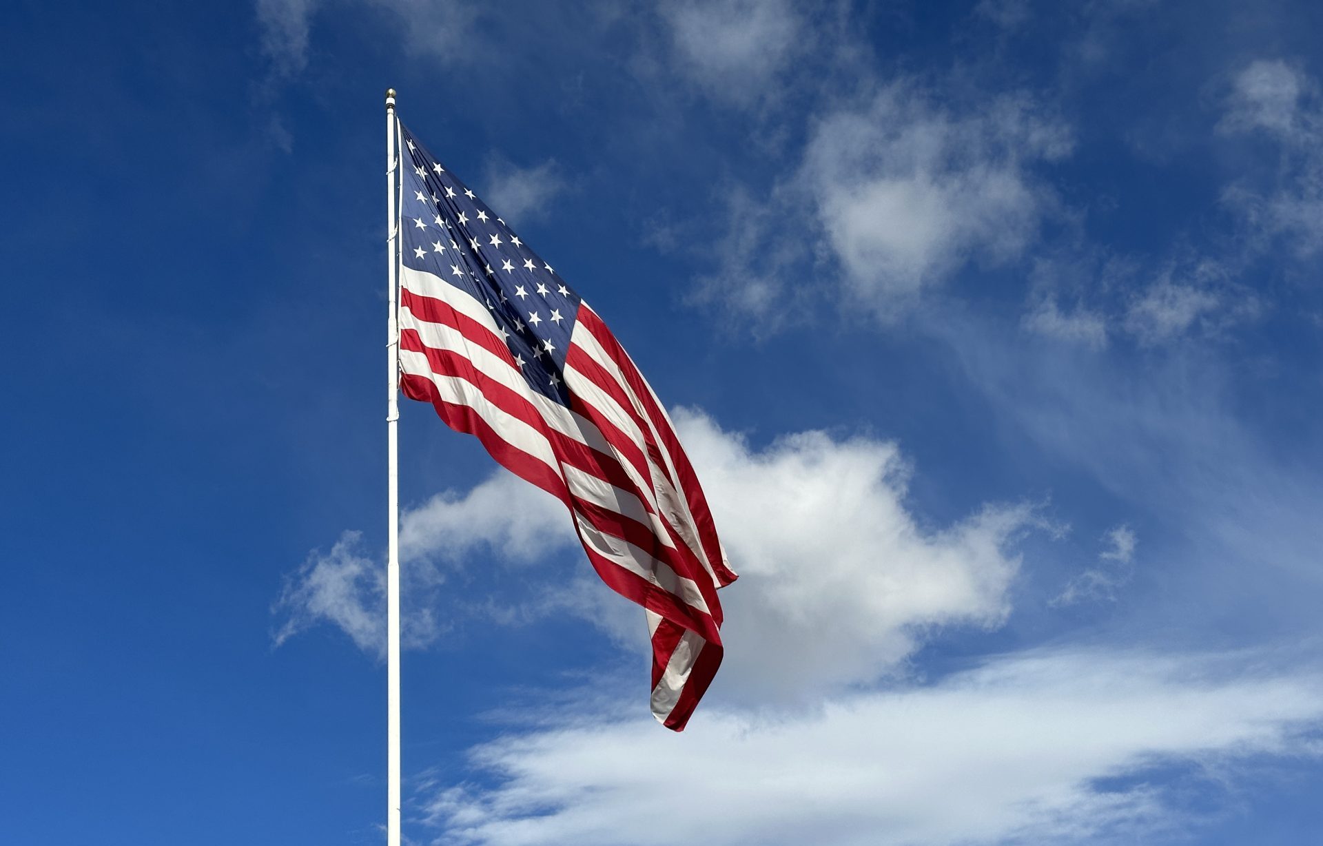 American flag blowing in the wind with a partly cloudy blue sky, USA